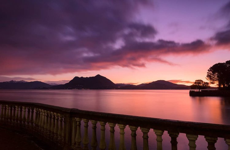 balconata su lago, tramonto dai colori viola rosa e arancio. montagne sullo sfondo