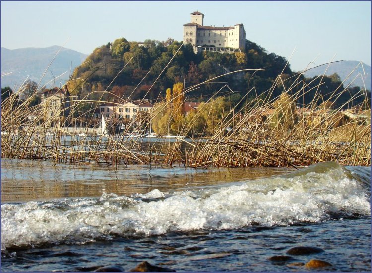 onde del lago che battono sulla battigia. canneto. castello di angera in cima alla verde rocca borromea