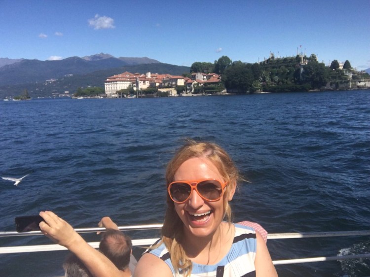 ragazza occhiali da sole arancioni, lago blu, isola borromeo sullo sfondo, giardino all'italiana